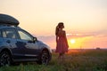 Silhouette of female driver standing near her car on grassy field enjoying view of bright sunset. Young woman relaxing during road Royalty Free Stock Photo