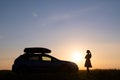 Silhouette of female driver standing near her car on grassy field enjoying view of bright sunset. Young woman relaxing Royalty Free Stock Photo