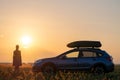 Silhouette of female driver standing near her car on grassy field enjoying view of bright sunset. Young woman relaxing Royalty Free Stock Photo