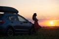 Silhouette of female driver standing near her car on grassy field enjoying view of bright sunset. Young woman relaxing Royalty Free Stock Photo