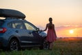 Silhouette of female driver standing near her car on grassy field enjoying view of bright sunset. Young woman relaxing Royalty Free Stock Photo