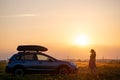 Silhouette of female driver standing near her car on grassy field enjoying view of bright sunset. Young woman relaxing Royalty Free Stock Photo