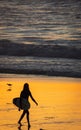 Silhouette female holding a surfboard walking on sunset golden beach by the sea Royalty Free Stock Photo