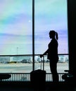 SILHOUETTE: Female passenger looking through the large window before her flight. Royalty Free Stock Photo