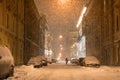 People walking along parked cars on empty evening city street during a snowstorm in winter Royalty Free Stock Photo