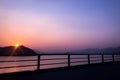 Silhouette of fence, mountain, ocean and sun at sunset