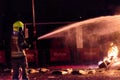 Silhouette of fireman trying to control a fire in a street during a night