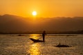 The silhouette of a fisherman on a boat at dusk The sunset is a beautiful orange sky