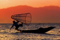 Silhouette of a fisherman in a boat with traditional Intha conical net in Myanmar