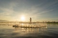 Silhouette Fisherman casting or throwing a net for catching freshwater fish in nature lake or river with reflection in morning