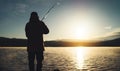 Silhouette fisherman with fishing rod at sunrise sunlight, outline man enjoy hobby sport on evening lake, person catch fish Royalty Free Stock Photo