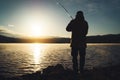 Silhouette fisherman with fishing rod at sunrise sunlight, outline man enjoy hobby sport on evening lake, person catch fish