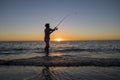 Silhouette of fisherman with hat on the beach with fish rod standing on sea water fishing at sunset with beautiful orange sky in v Royalty Free Stock Photo