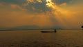 Silhouette fisherman with rowboat, dramatic sunset on the lake, beautiful peaceful scene, bright sun light. Royalty Free Stock Photo