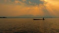 Silhouette fisherman with rowboat, dramatic sunset on the lake, beautiful peaceful scene, bright sun light. Royalty Free Stock Photo