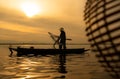 Silhouette of fisherman at sunrise, Standing aboard a rowing boat and casting a net to catch fish
