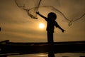 Silhouette of fisherman at sunrise, Standing aboard a rowing boat and casting a net to catch fish