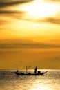 Silhouette of fishermen in the boat on sea with yellow and orange sun in the background