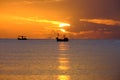 Silhouette of a fishing boat sailing on the ocean water at sunset with golden light reflected on the water surface and soft waves Royalty Free Stock Photo