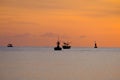 Silhouette of a fishing boat sailing on the ocean water at sunset with golden light reflected on the water surface and soft waves Royalty Free Stock Photo