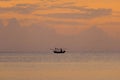 Silhouette of a fishing boat sailing on the ocean water at sunset with golden light reflected on the water surface and soft waves Royalty Free Stock Photo