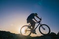 Silhouette of a fit male mountain biker riding his bike uphill on rocky harsh terrain on a sunset