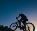 Silhouette of a fit male mountain biker riding his bike uphill on rocky harsh terrain on a sunset