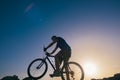 Silhouette of a fit male mountain biker riding his bike uphill on rocky harsh terrain on a sunset