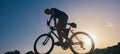 Silhouette of a fit male mountain biker riding his bike uphill on rocky harsh terrain on a sunset