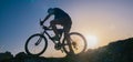 Silhouette of a fit male mountain biker riding his bike uphill on rocky harsh terrain on a sunset