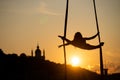 Silhouette of a flexible woman acrobat on aerial silk during a sunset on Kiev city background. concept of freedom and