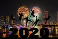 Silhouette of friends jumping celebrating new year over number 2020 on blurred city and river with fireworks background Royalty Free Stock Photo