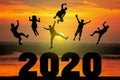 Silhouette of friends jumping celebrating new year over number 2020 on blurred sunrise background Royalty Free Stock Photo