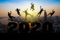 Silhouette of friends jumping celebrating new year over number 2020 on top of building on blurred city and sunrise background Royalty Free Stock Photo