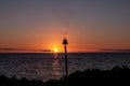 A silhouette of a gas torch with flame rising up against a sunset over Pacific ocean.