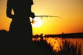 Silhouette of a girl with a fishing rod on the river bank at dawn Royalty Free Stock Photo