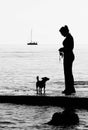 Silhouette of a girl with her dog on the beach with boat sailing in background Royalty Free Stock Photo