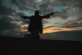 Silhouette of a girl on her knees and arms outstretched at sunset