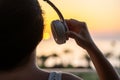 Silhouette of girl listening music in headphones standing on balcony and looking at sunset palm sea beach. Rear view of female. Royalty Free Stock Photo