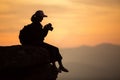 Silhouette girl photographer sitting on the rocks at high shooting at sunset. Royalty Free Stock Photo