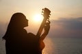 Silhouette of girl playing the guitar on the background of the sea and a beautiful sunset Royalty Free Stock Photo