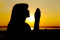 Silhouette of a girl raises hands to God