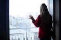 Silhouette Of A Girl In A Red Sweater Near The Window And City View. Depression And Loneliness. Toned