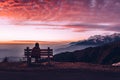 Silhouette of a Girl sitting on bench at Sunset - Girl looking at Snow Capped Mountains with Orange Scattered Clouds in the Sky Royalty Free Stock Photo