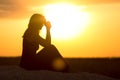 Silhouette of girl sitting on the sand and praying to God at sunset, the figure of young woman on the beach, concept religion