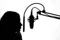 Silhouette of a girl with a studio microphone, radio presenter, singer and blogger, voice acting for films. Strong, black and Royalty Free Stock Photo