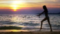 Silhouette of a girl at sunset, against the background of the sea, slender leggy girl funny doing gymnastic coups on the Royalty Free Stock Photo