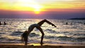 Silhouette of a girl at sunset, against the background of the sea, slender leggy girl funny doing gymnastic coups on the Royalty Free Stock Photo