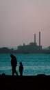 Silhouette of grandfather and grandson looking at a factory in the other side of the river