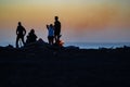 In silhouette, group of beach-goers after sunset enjoying a beach barbeque and summer evening